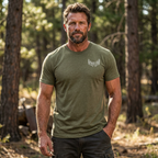 Man standing in a field and forest edge wearing the Back 40 League Whitetail Classic Tee in heather olive – front view men’s whitetail hunting shirt