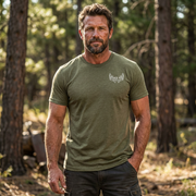 Man standing in a field and forest edge wearing the Back 40 League Whitetail Classic Tee in heather olive – front view men’s whitetail hunting shirt