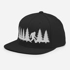 Front left view of black trucker hat featuring a white embroidered Bigfoot silhouette walking through pine trees.