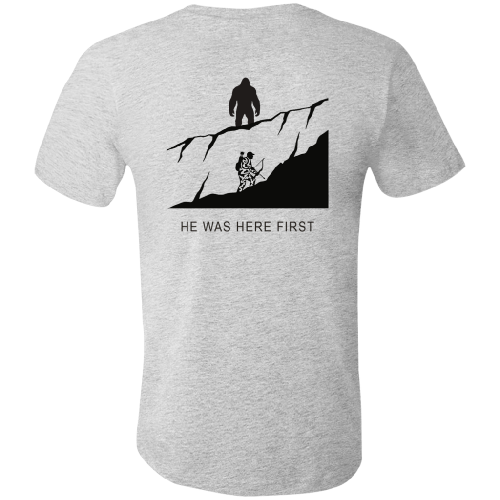 Back view of the Men’s He Was Here First Bigfoot Hunting Tee in Athletic Heather showing a large graphic of Bigfoot standing on a ridge above a climbing bowhunter with He Was Here First text.