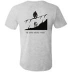 Back view of the Men’s He Was Here First Bigfoot Hunting Tee in Athletic Heather showing a large graphic of Bigfoot standing on a ridge above a climbing bowhunter with He Was Here First text.