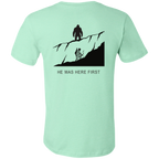 Back view of the Men’s He Was Here First Bigfoot Hunting Tee in Heather Mint showing a large graphic of Bigfoot standing on a ridge above a climbing bowhunter with He Was Here First text.