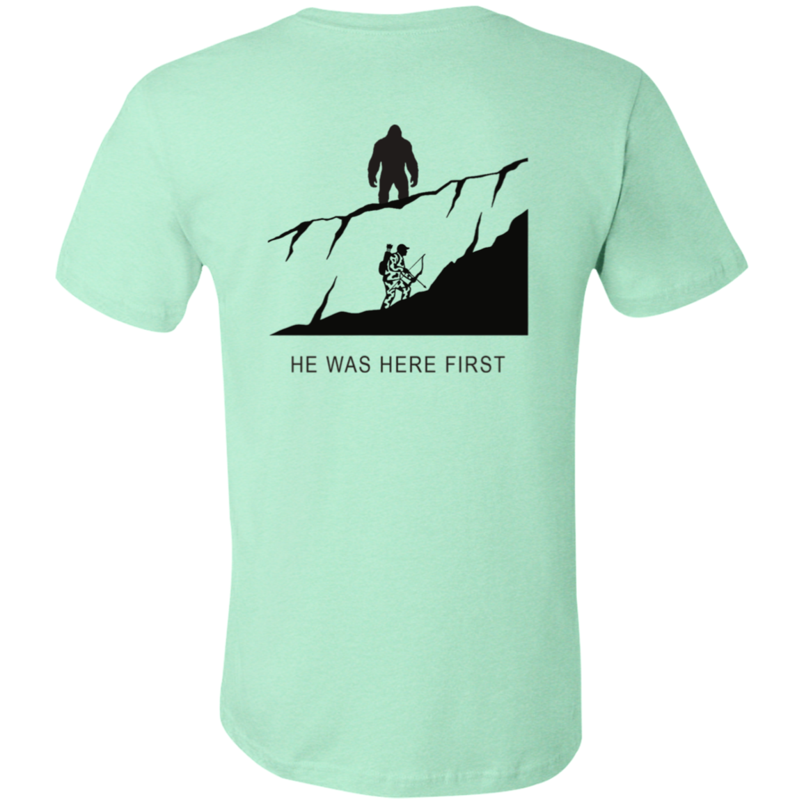 Back view of the Men’s He Was Here First Bigfoot Hunting Tee in Heather Mint showing a large graphic of Bigfoot standing on a ridge above a climbing bowhunter with He Was Here First text.