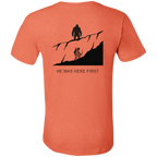 Back view of the Men’s He Was Here First Bigfoot Hunting Tee in Heather Orange showing a large graphic of Bigfoot standing on a ridge above a climbing bowhunter with He Was Here First text.