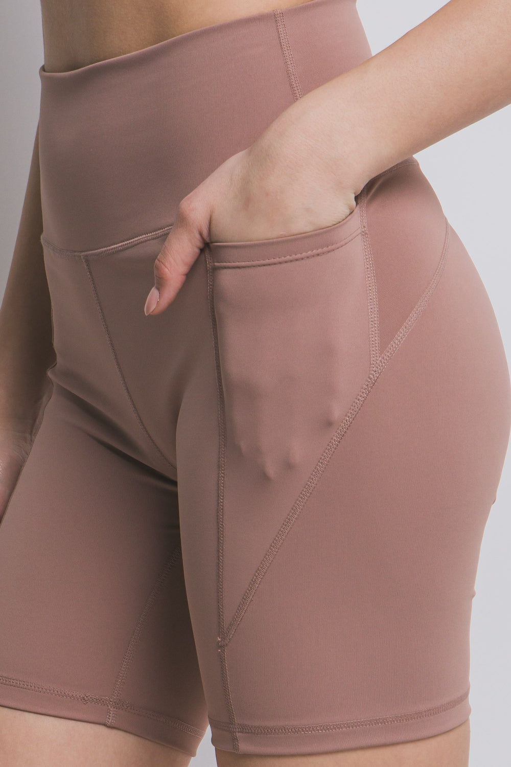 Left Side of High Waist Seam Detail Active Shorts in Taupe, woman placing hand in pocket blank with no graphics or text. 