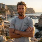 Model outdoors wearing grey mens hunting graphic tee with Fearless Harbor Buck Logo design at front in rugged outdoor setting.