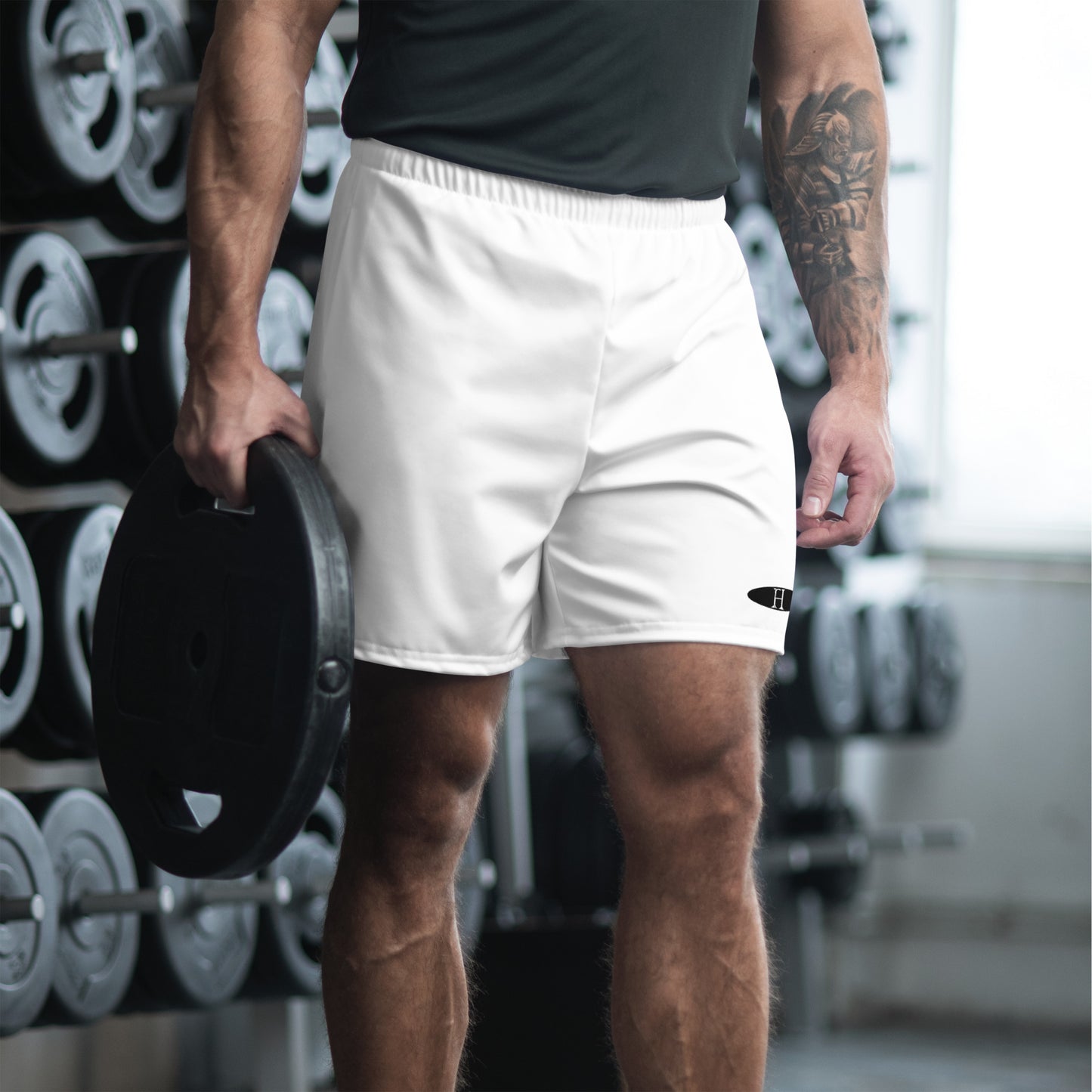 Front of man wearing Athletic Training 6.5 Shorts in White, at gym and carrying large weight plate, FH logo on bottom right.