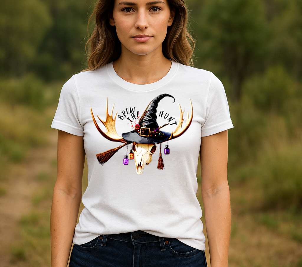 Front view of Woman Wearing Brew the Hunt Tee in White, featuring skull with antlers, witch hat, and broomstick design.