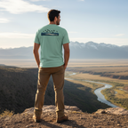 Man outdoors wearing the Men's Drift Line Waterfowl Tee in Heather Prism Dusty Blue showing ducks flying over marsh horizon graphic