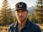 Man outdoors wearing a mens navy white elk hunting trucker hat with elk crest embroidered on the front