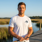 Man outdoors, holding a fishing rod, wearing the Men's First Light Waterfowl Tee in White front view with Public Marsh emblem