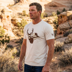 Man outdoors wearing the Men's Mesa Mule Deer Tee in Heather Dust with the High Desert Rack mule deer emblem on the left sleeve