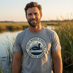 Man outdoors wearing the grey triblend Public Marsh Syndicate waterfowl tee with coot chest emblem