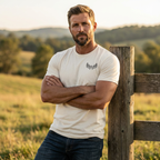 Man outdoors wearing the Men's Scrape Circle Whitetail Staple Tee in Heather Dust front view showing the chest emblem in a natural hunting lifestyle setting